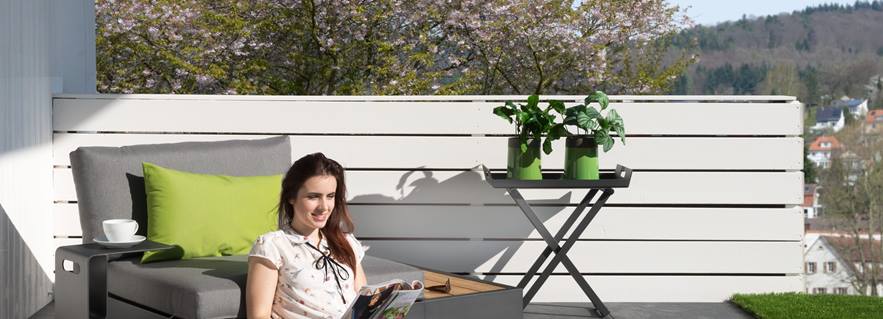 Vrouw zittend op terras met grijze platen en modern meubilair